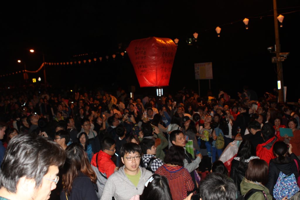 Balão caracterizado com frases de desejos indo ao céu em meio a multidão.